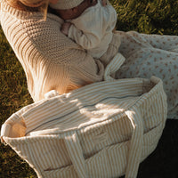 femme tient un bébé et un sac
à couches rayé jaune est par terre