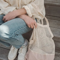 femme assise dans les marches avec un sac en filet au bras