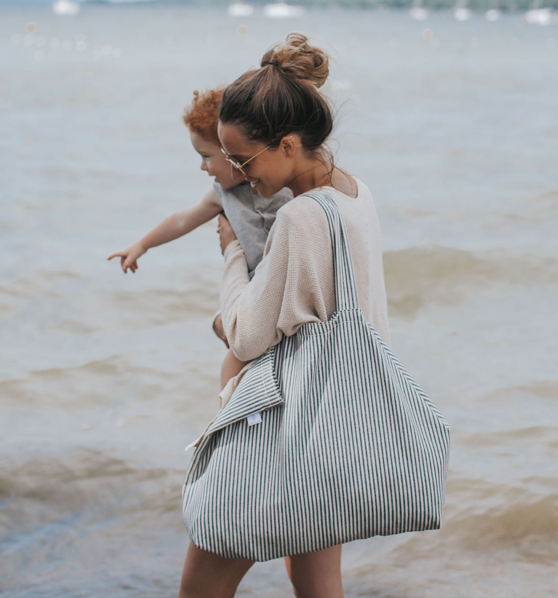 femme marche avec enfant dans les bras et porte un sac rayé bleu sur l'épaule