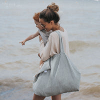 femme marche avec enfant dans les bras et porte un sac rayé bleu sur l'épaule