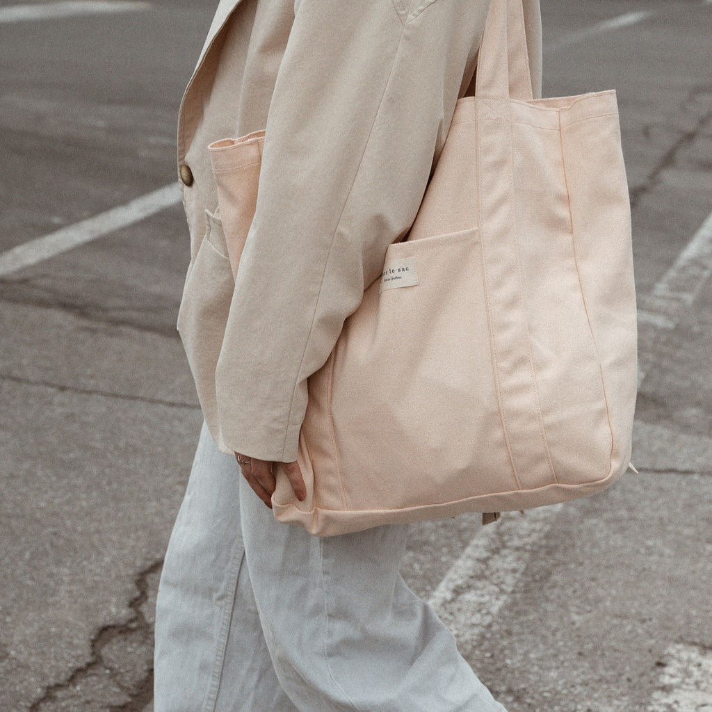 femme marchant dans la rue avec un sac fourre tout de la mrque Dans le sac à l'épaule de couleur pêche
