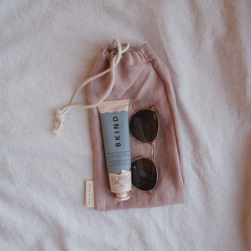 petit sac en lin rose avec lunettes soleil et tube de crème