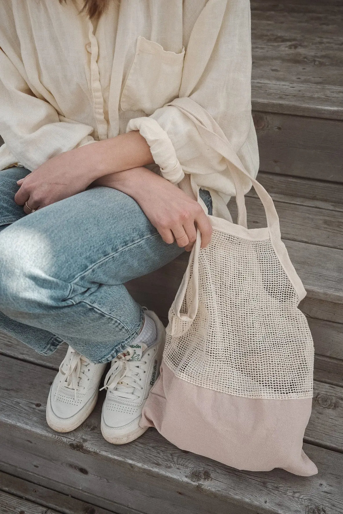 femme assise dans les marches avec un sac en filet au bras