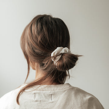 femme de dos les cheveux attachés par un élastique à cheveux chouchou en coton de couleur ivoire