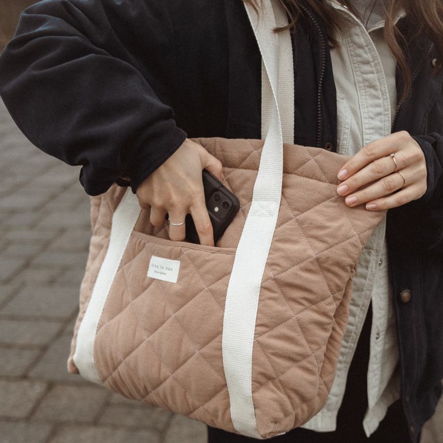 femme qui glisse son téléphone dans la pochette avant d sac fourre-tout matelassé Tan