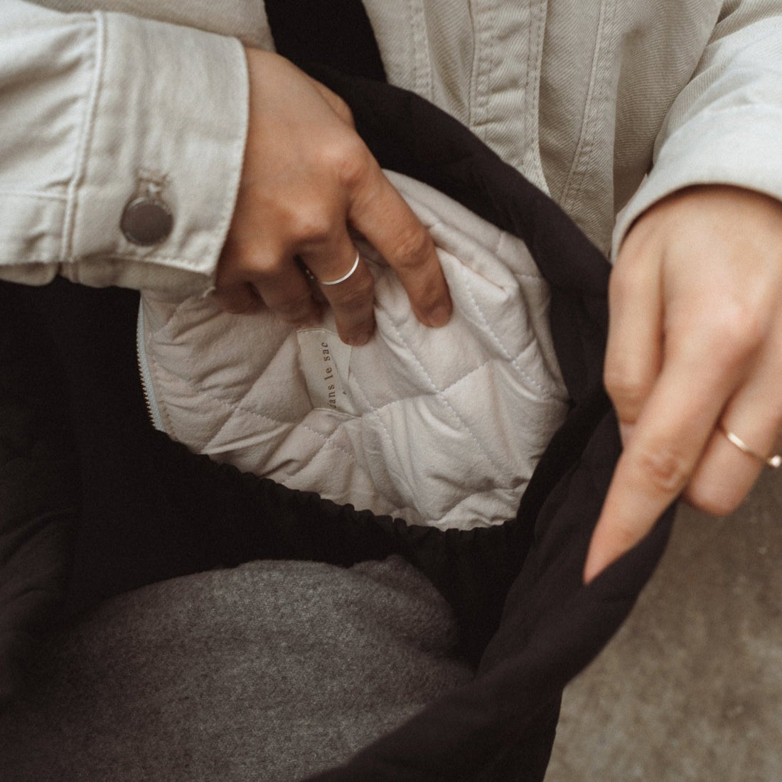 une personne range une pochette matelassée dans la pochette intérieure du fourre-tout noir