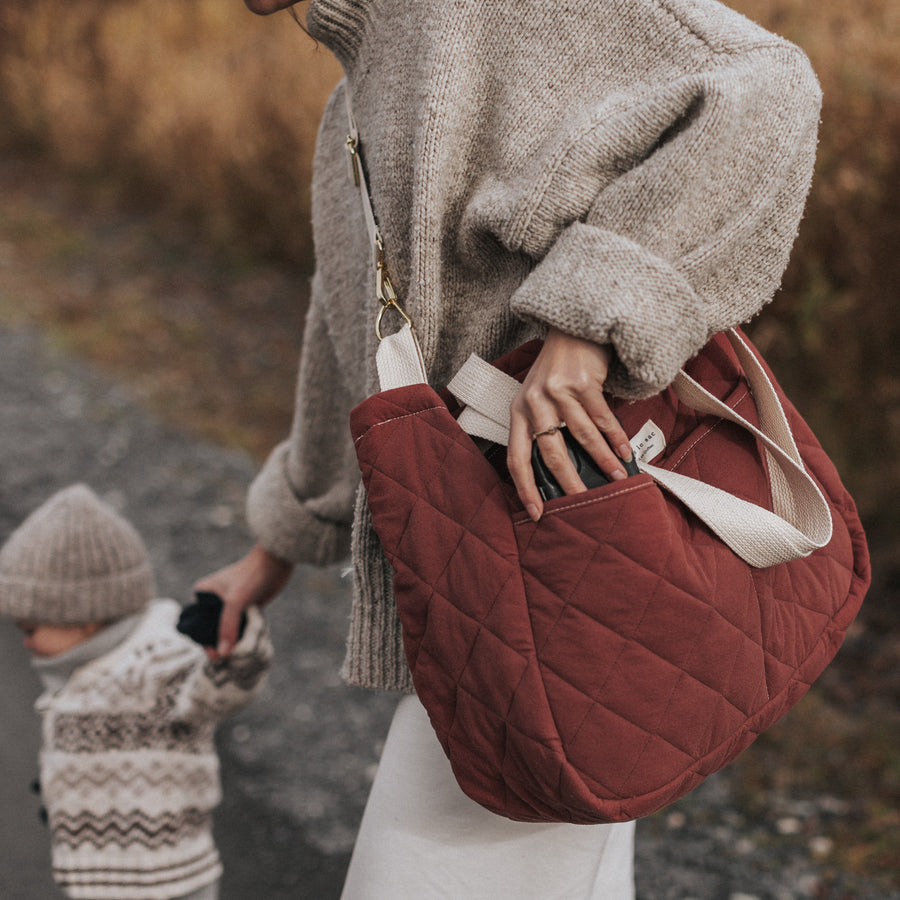 femme porte un sac à couche à l'épaule et tien un enfant par la main