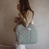 femme tien un enfant dans ses bras et porte un sac à couche vert menthe à l'épaule